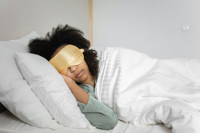 A woman peacefully sleeping with an eye mask in a cozy white bedroom setting.